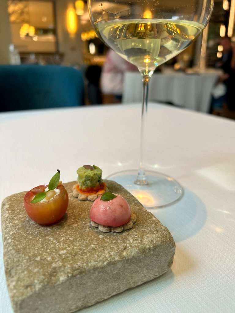 A small plated dish on a stone slab beside a glass of white wine